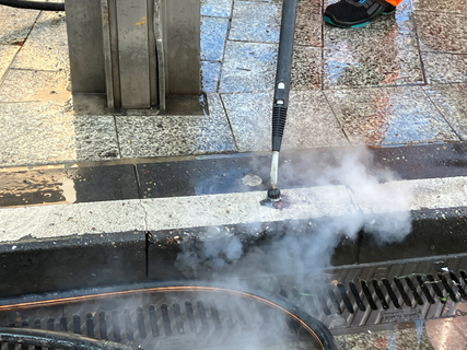 Die Düse des GumFree-Reinigungsgeräts sprüht Dampf auf einen Kaugummi, der auf dem Boden festgetreten ist.