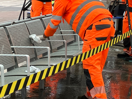 Ein Mann putzt eine Sitzbank an der Haltestelle Berliner Platz mit einem Lappen.