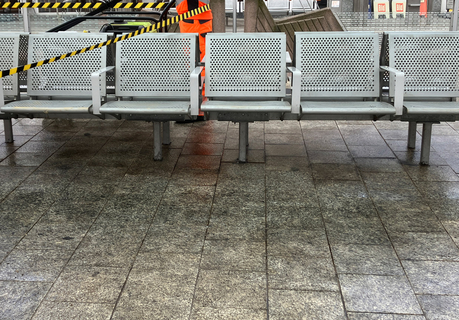 Eine Sitzbank an der Haltestelle Berliner Platz nach der Haltestellenreinigung. Auf den Bodenplatten ist deren ursprüngliche Farbe zu erkennen. Die Farbe ist weiß mit dunklen Sprenkeln.