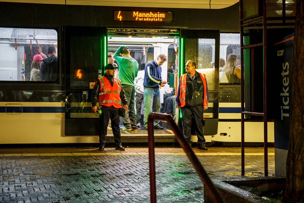 Zwei Mitarbeiter der rnv stehen in Warnweste vor den geöffneten Türen einer Straßenbahn vom Typ RNT an einer Haltestelle.