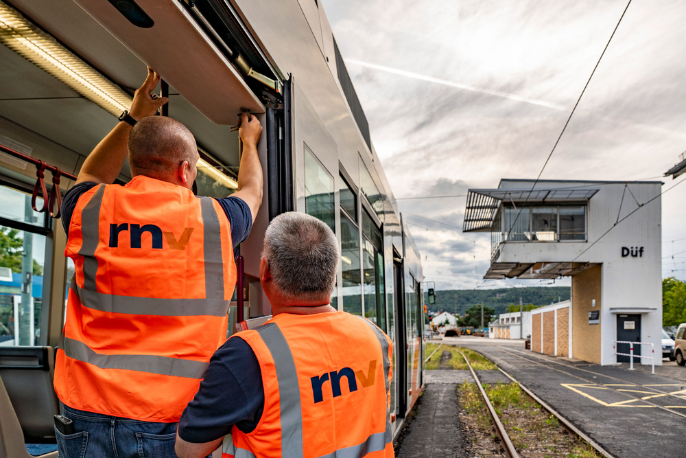 Zwei rnv-Mitarbeiter arbeiten an der geöffneten Tür einer Straßenbahn