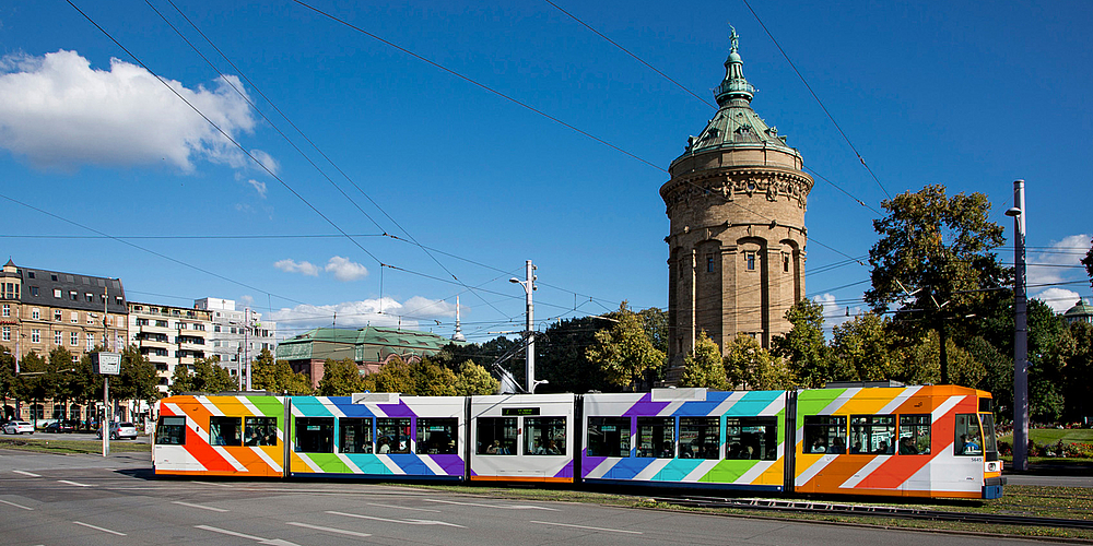 rnv-Bahn in Regenbogenfarben vor Mannheimer Wasserturm