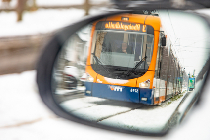Im Rückspiegel eines Autos fährt eine Straßenbahn über verschneite Gleise