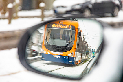 Im Rückspiegel eines Autos fährt eine Straßenbahn über verschneite Gleise