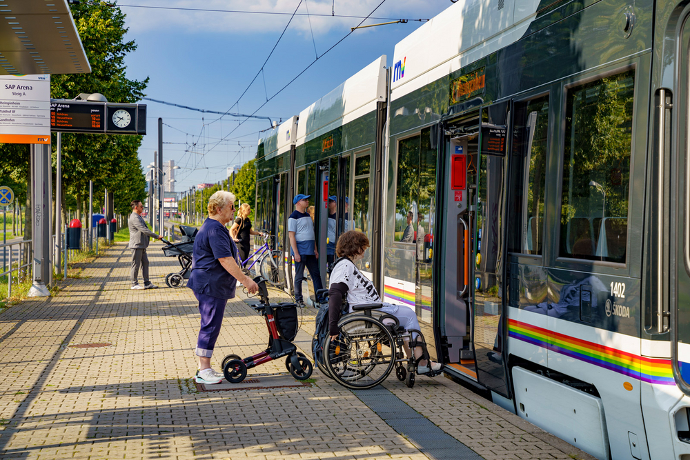 Eine Rhein-Neckar-Tram steht an der Haltestelle SAP-Arena. Eine Frau mit Rollator, eine Frau im Rollstuhl, eine Frau mit Fahrrad und ein Mann mit Kinderwagen steigen ein.