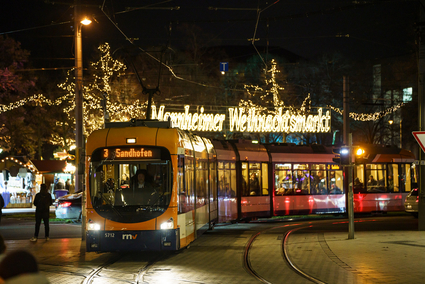 Eine Stadtbahn des Typ Rhein-Neckar-Vario fährt in die Haltestelle Wasserturm ein, mit dem Weihnachtsmarkt Mannheim im Hintergrund.