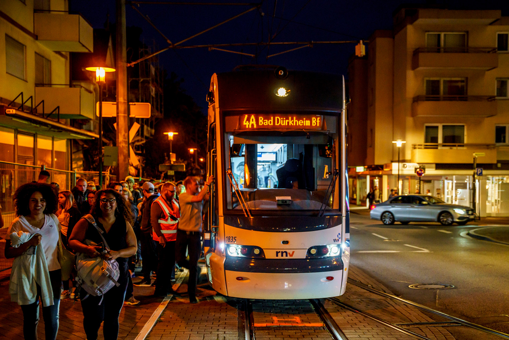 Eine Straßenbahn vom Typ RNT steht zum Wurstmarkt an der Haltestelle Bad Dürkheim Bahnhof. Viele Wurstmarkt-Besuchende steigen aus.