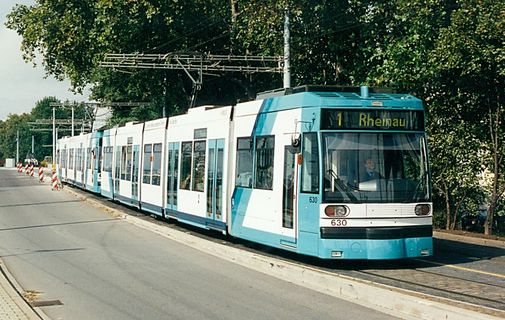 Zwei zu einer Doppeltraktion zusammengekuppelte Straßenbahnen fahren den sogenannten Beckebuckel hinab. Im Hintergrund sind viele große Bäume zu sehen.